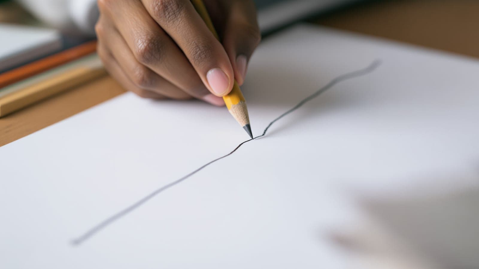 An Indian student's hand drawing a freehand perspective line across a page, no ruler anywhere on the desk