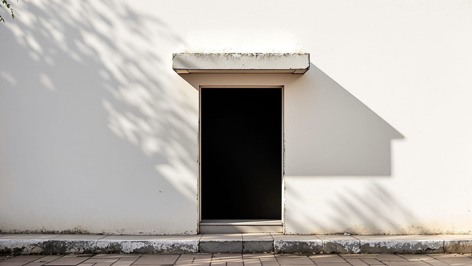 A whitewashed Indian courtyard wall in strong afternoon light, the shadow of a chajja merging with an open doorway into one connected dark shape