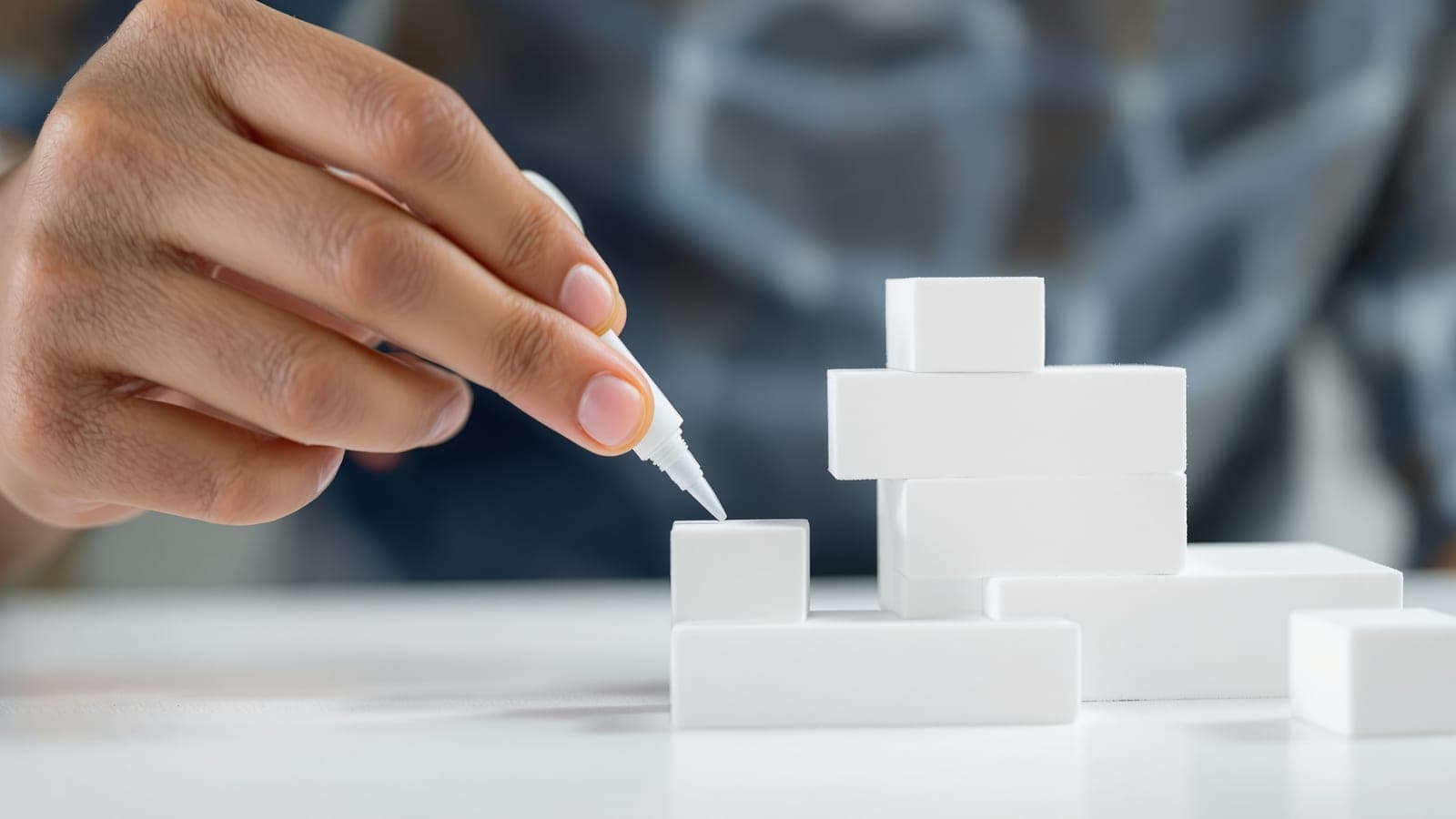 A hand poised over a foam composition holding a glue applicator, hesitating before committing