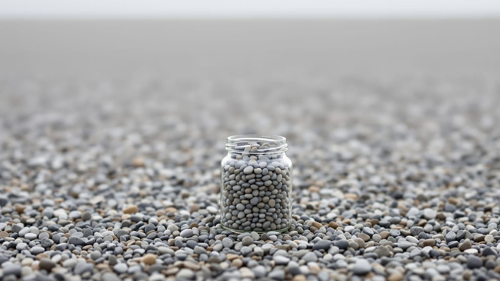 A glass jar filled with smooth pebbles standing on a vast shingle beach made of the same pebbles, stretching unbroken to the horizon