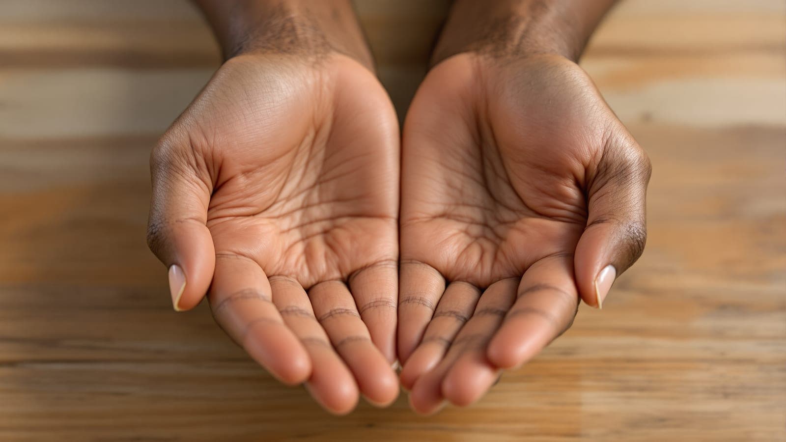 A pair of hands resting open and still on a completely bare wooden desk, with no paper, pen or device anywhere