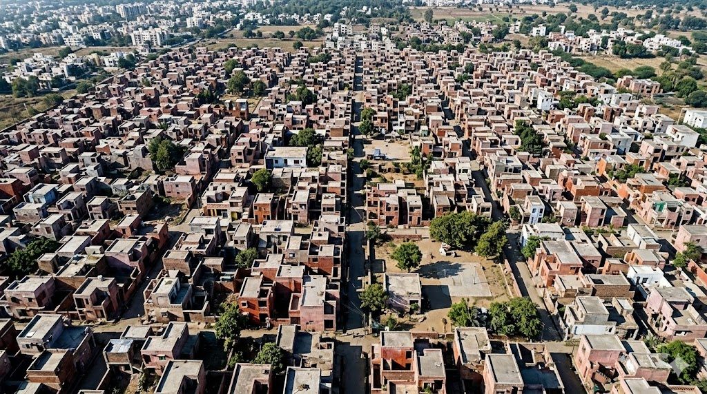 Aerial view of the Aranya low-cost incremental housing settlement near Indore, showing tightly clustered courtyard homes, narrow shaded streets and shared open spaces