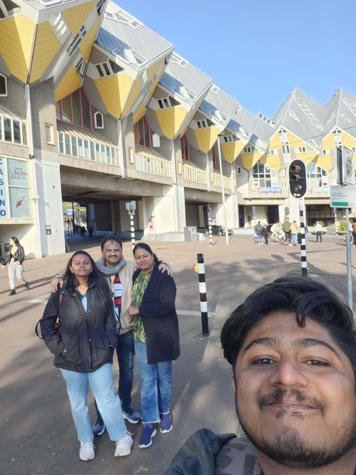Amogh taking a selfie with his family in front of the Cube Houses in Rotterdam, the tilted yellow cubes on their pylons rising behind them
