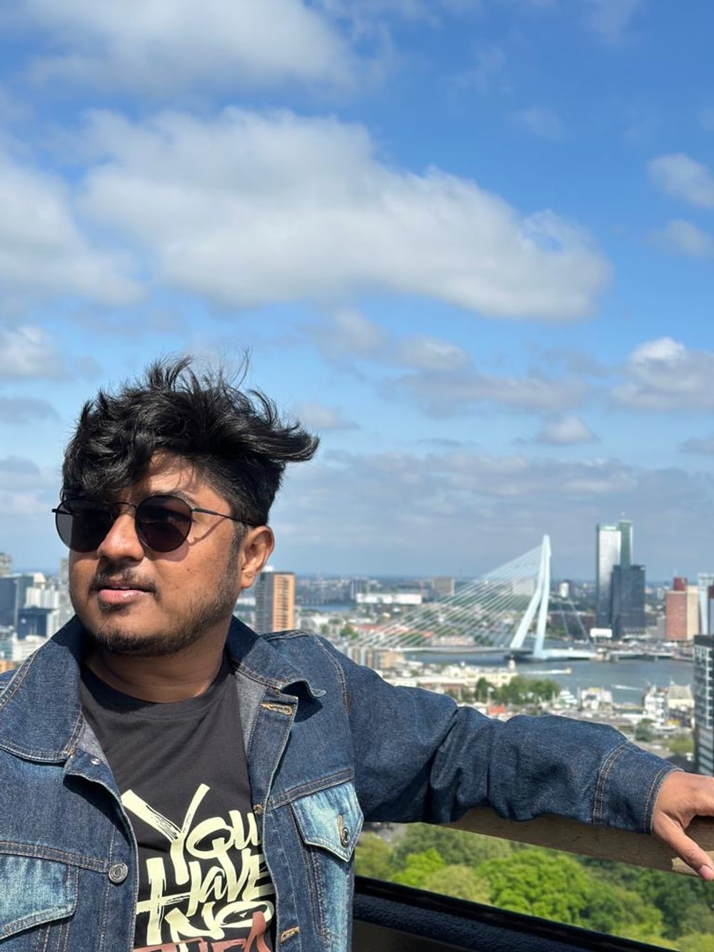 Amogh at a high viewpoint over Rotterdam, the white cable-stayed Erasmus Bridge and the city skyline on the Nieuwe Maas behind him