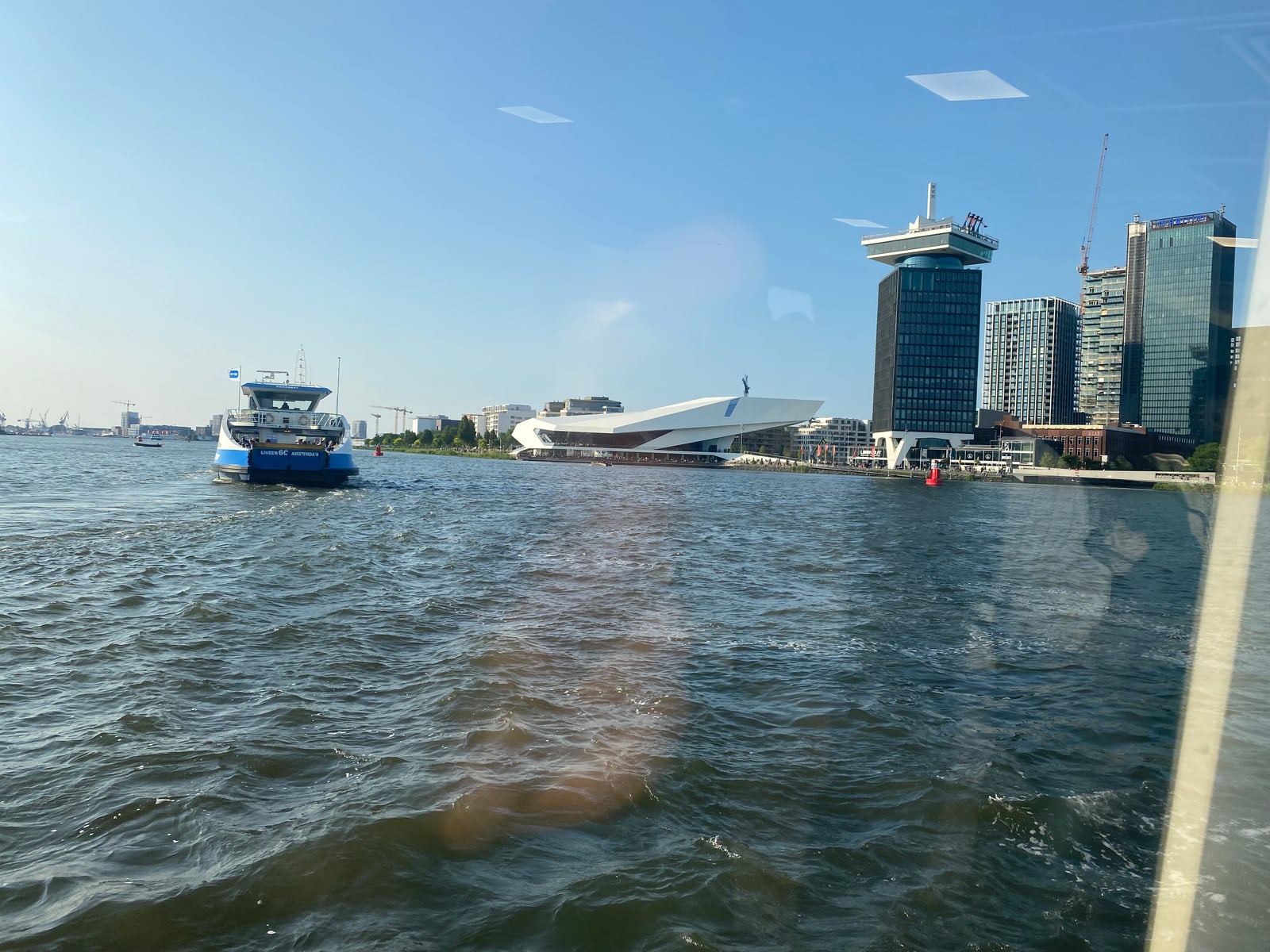 The EYE Filmmuseum and the A'DAM tower seen across the IJ from the Amsterdam ferry, the wide north-bank waterfront that Amogh photographed as he crossed the water