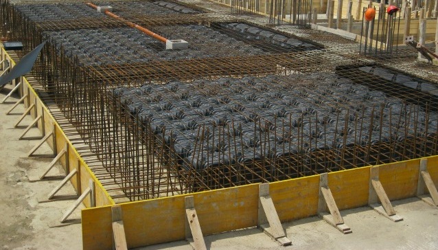 A suspended floor slab under construction: edge shuttering and timber formwork hold a steel reinforcement mesh in which rows of dark hollow void-formers have been laid to make a lightweight ribbed slab, all waiting to be concreted