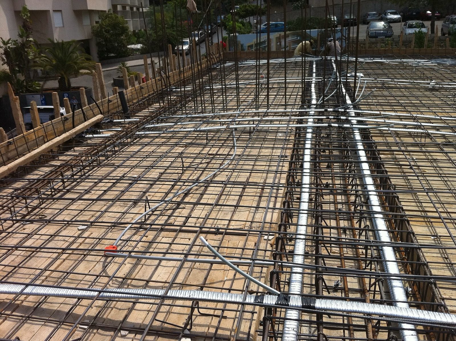 A suspended slab being reinforced before the pour, seen from above: two dense layers of steel bars are tied into a grid across the timber formwork, with beam cages running through the panels, exactly the steel that the layout and reinforcement sheets describe