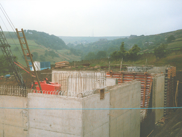 A reinforced-concrete structure under construction: a forest of vertical reinforcement starter bars rising from a freshly cast concrete element, with modular formwork and shuttering panels standing to one side on the open site — the physical reality the column layout drawing sets in motion