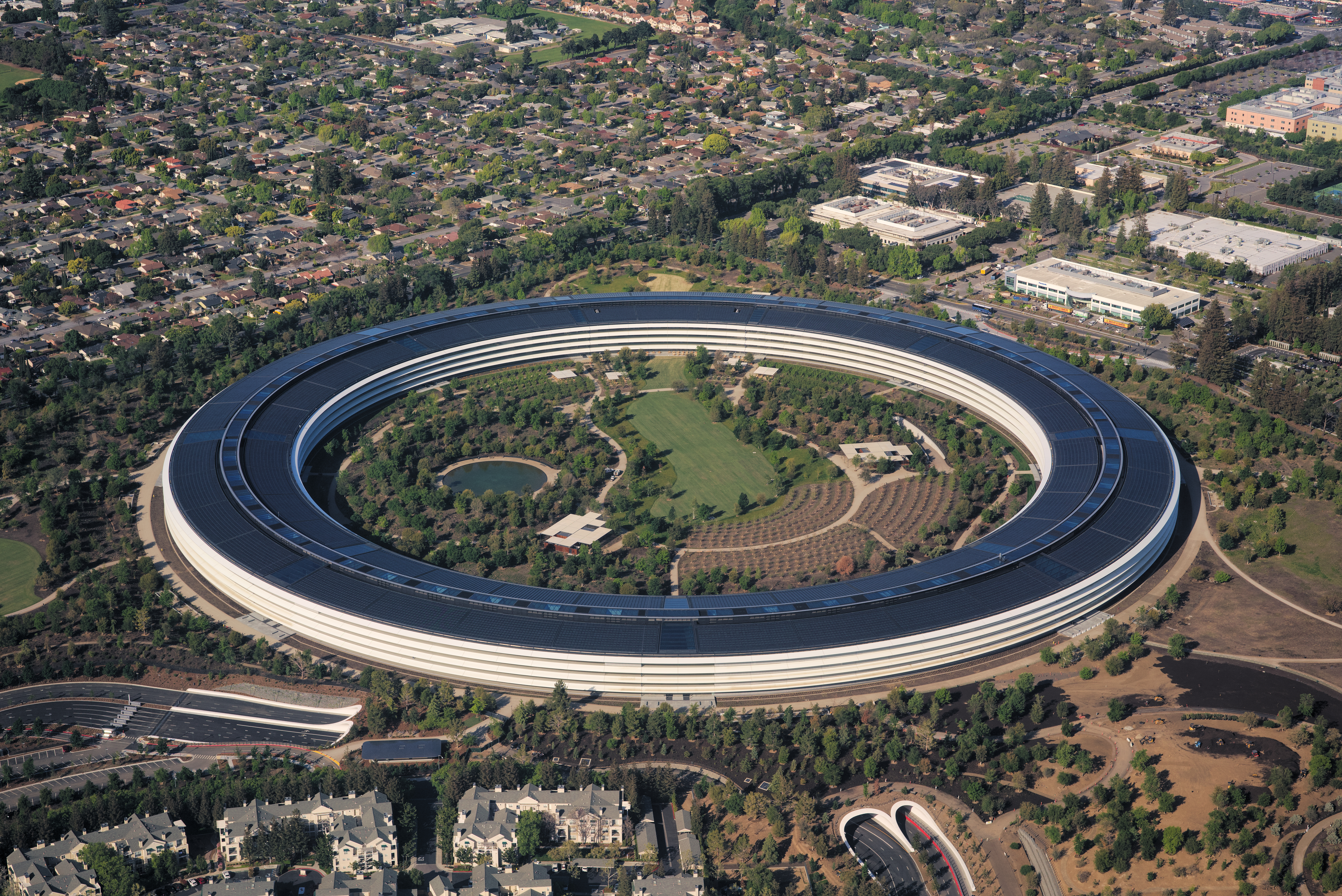 High-resolution aerial photograph of the complete Apple Park ring set in its landscaped campus, showing the circular form and central courtyard.