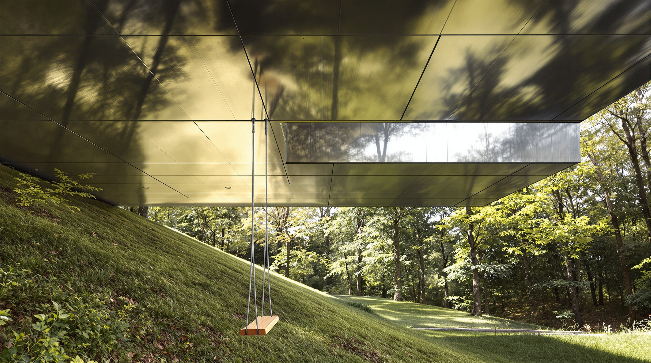 The Balancing Barn seen from below its cantilevered end, looking up at the underside of the projecting house and its reflective steel soffit, a simple swing hanging from the structure, with the descending grassy Suffolk slope and woodland falling away beneath