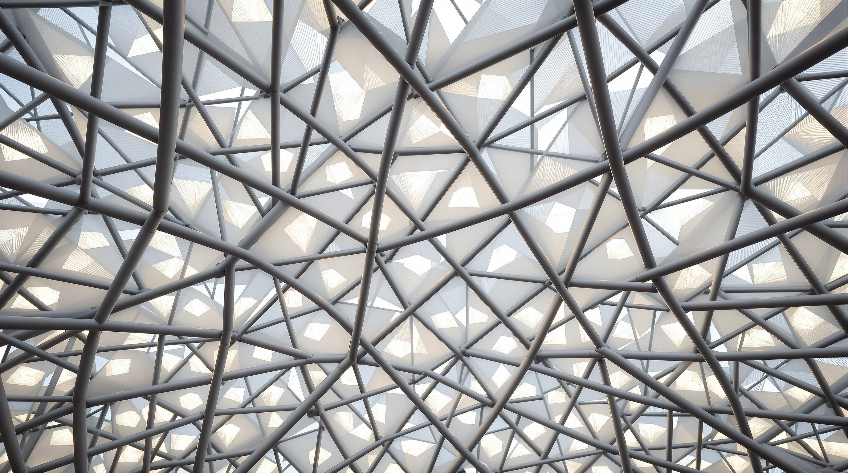 Looking straight up inside the Bird's Nest at the interwoven steel members crossing at every angle, the gaps between them filled with translucent white ETFE membrane cushions that glow against the sky, like light through the twigs of a real nest