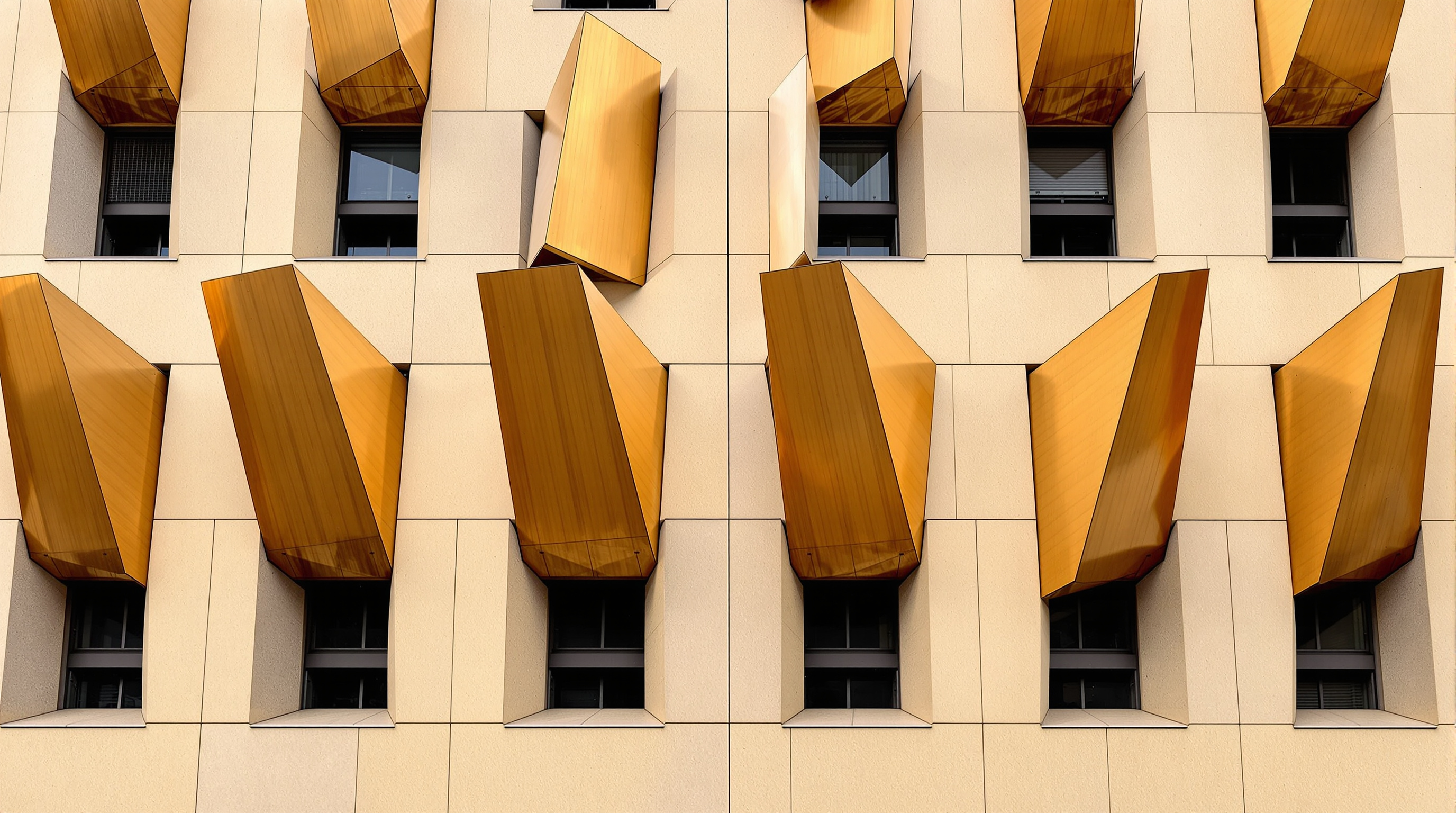 Close view of the Bloomberg facade: angled blade-like bronze ventilation fins projecting from honey-coloured sandstone, some panels tilted open to reveal dark ventilation slots behind, warm metal against pale stone