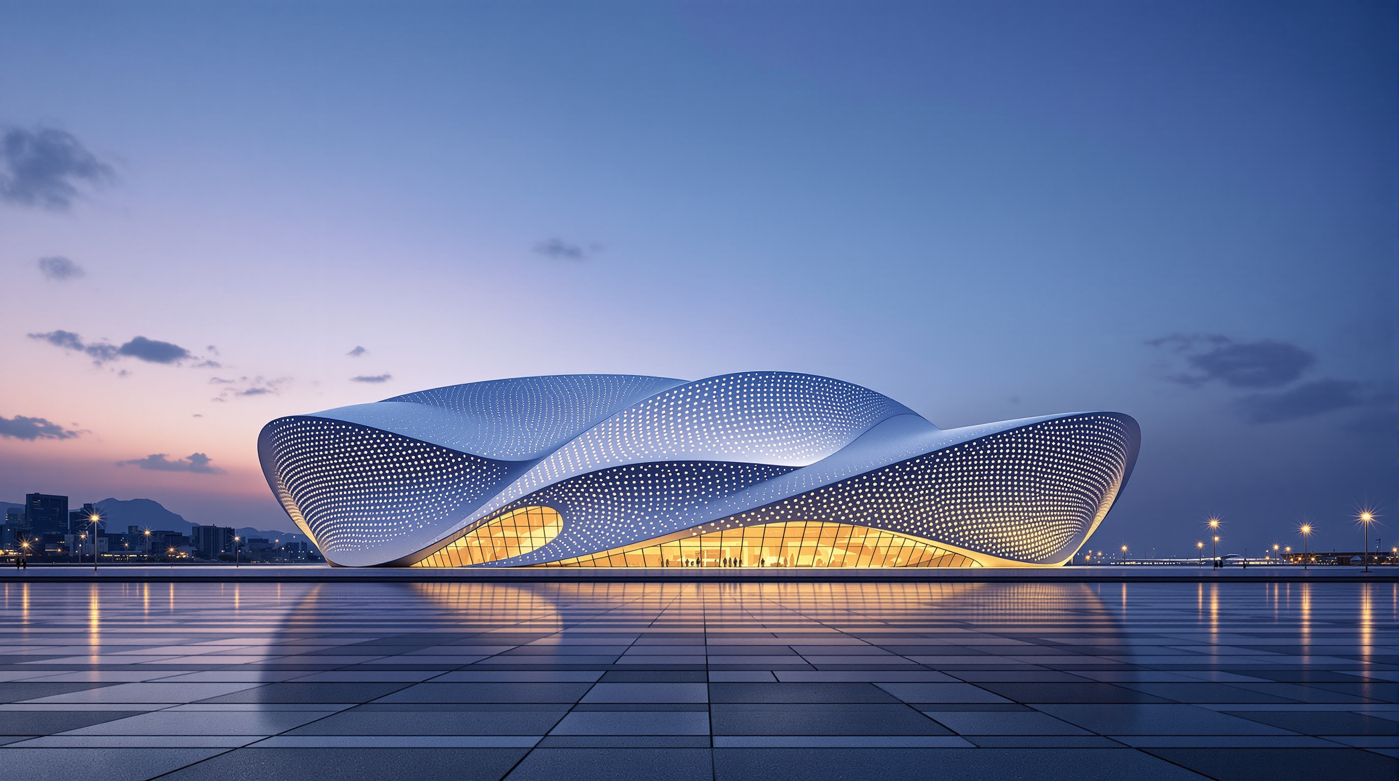 Wide dusk view of the Dalian International Conference Center glowing from within, its perforated silver shell lit against the harbour, the building standing somewhat isolated on a broad reclaimed waterfront esplanade with few people in the foreground