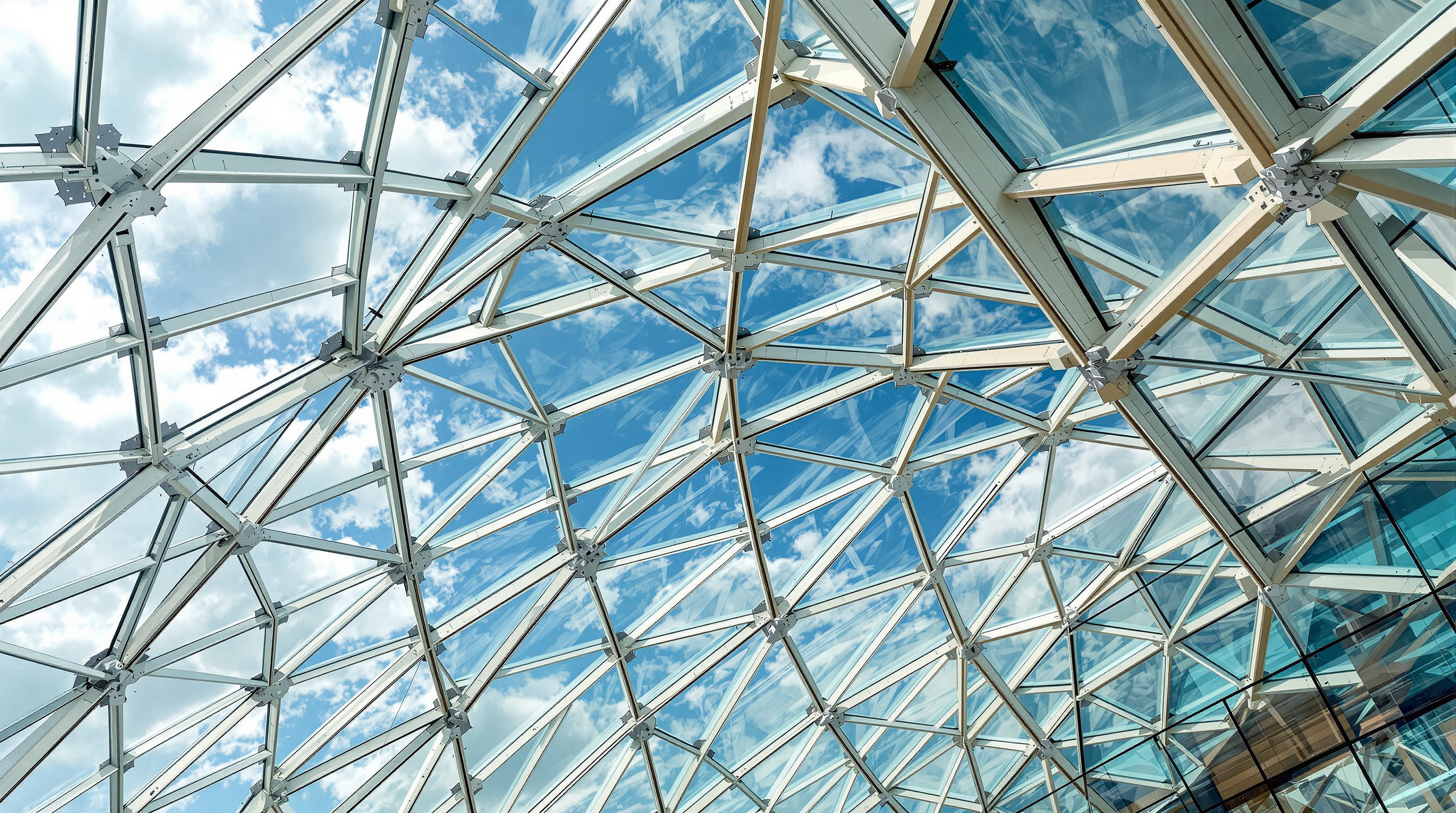 Detail of the Fondation's glass sails from below, curved laminated glass panels held in a fine web of steel and pale glued-laminated timber beams that twist and fan across the sky, the joints and node connections crisply visible against bright cloud