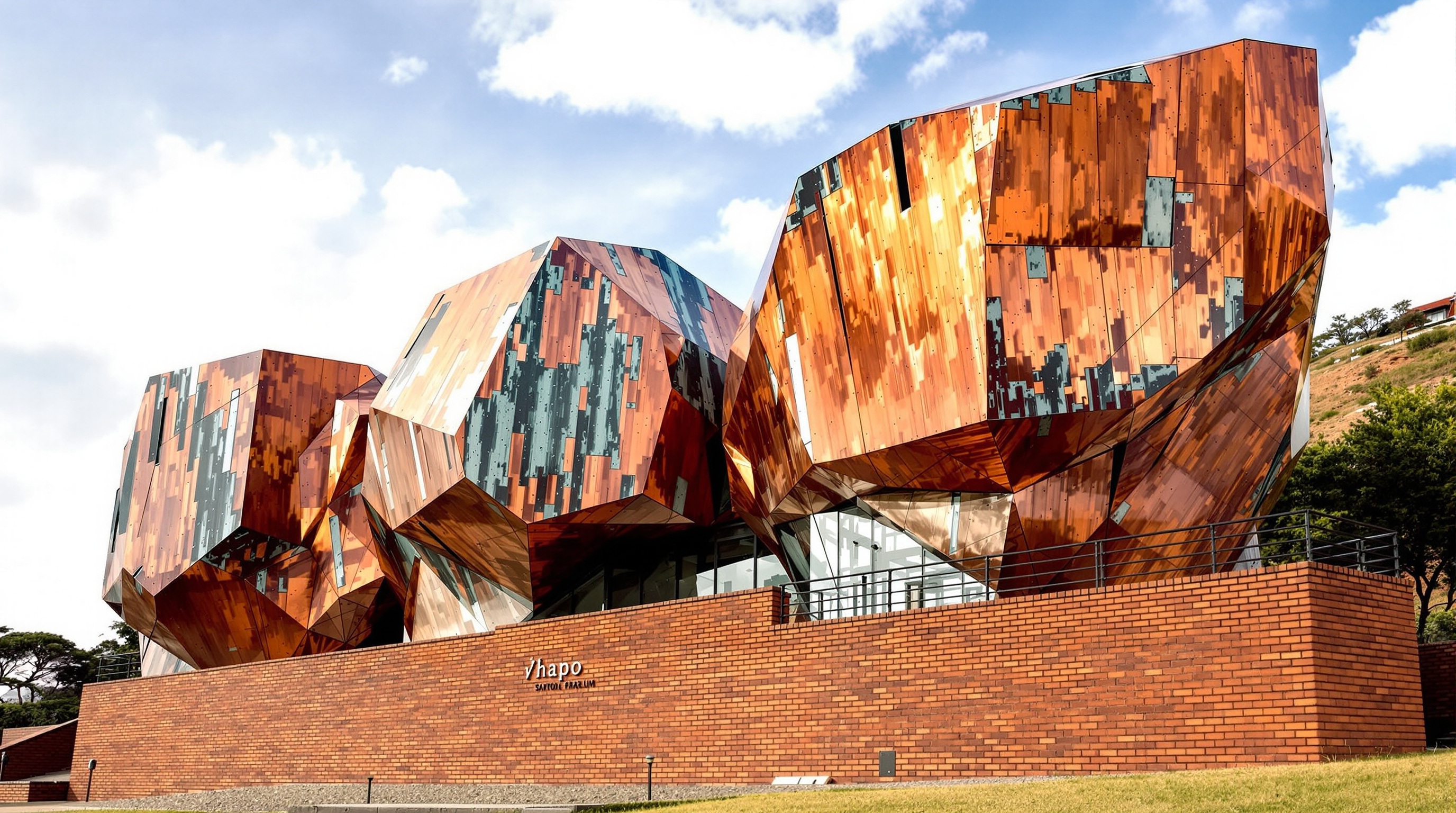 The //hapo museum at Freedom Park seen from below: angular, copper-clad boulder-like volumes rising from a red-brick plinth at the foot of Salvokop hill, the metal surface streaked where it has begun to weather toward green, narrow crevices cut into the forms