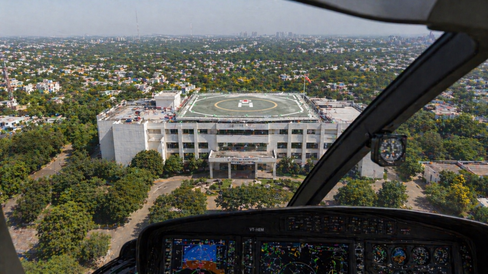 Helicopter pilot's-view approach to a hospital helipad — surrounding buildings cleared from the 8° obstacle cone, painted yellow target visible below