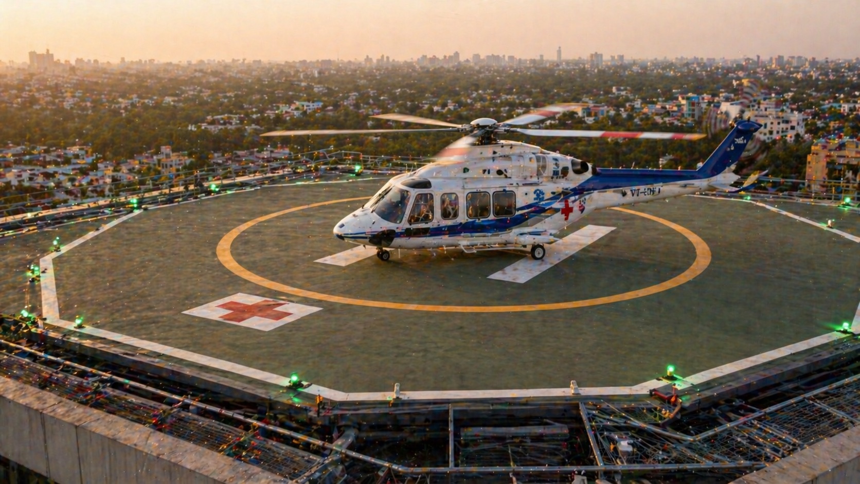 Rooftop helipad with medium-class helicopter just landed — painted yellow target, perimeter green lights, raised steel-frame deck above hospital