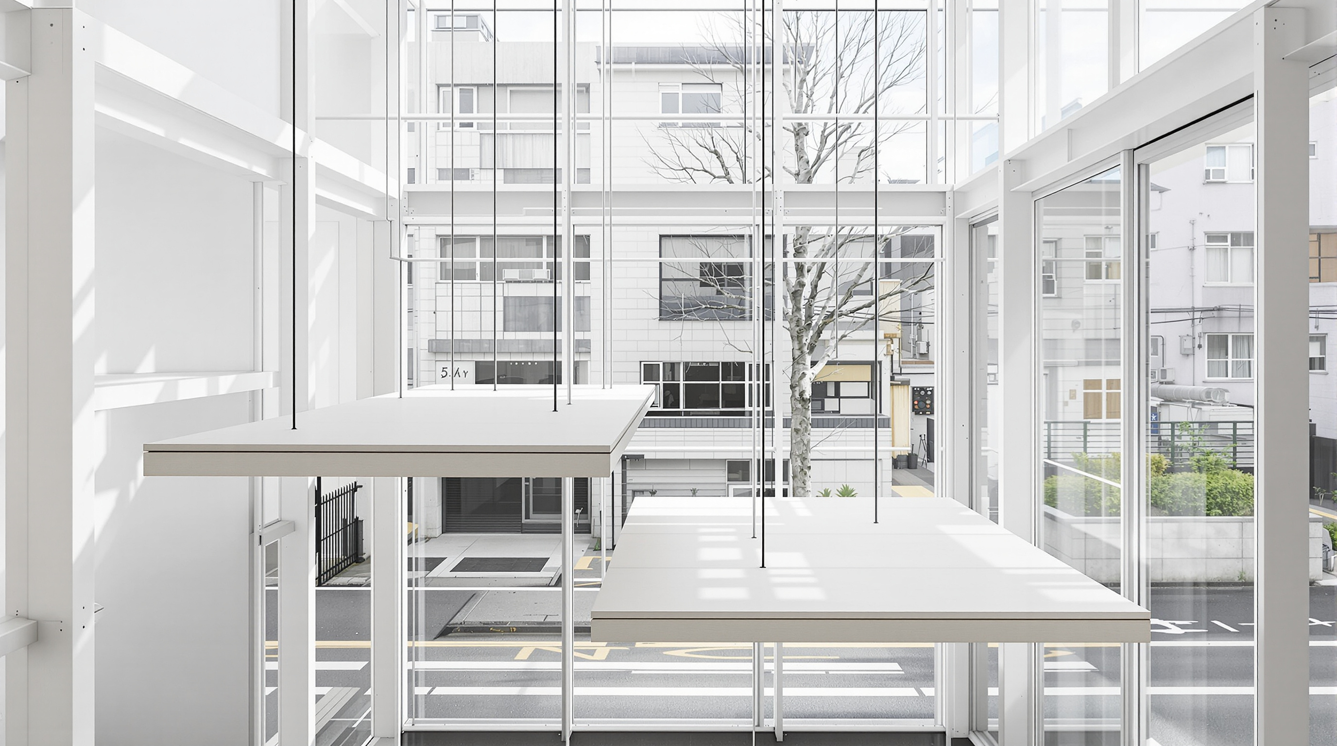 Interior of House NA looking up through the white steel frame, showing several small pale timber floor plates floating at different heights, a short ladder linking two of them, and the glass wall revealing the neighbouring Tokyo street beyond