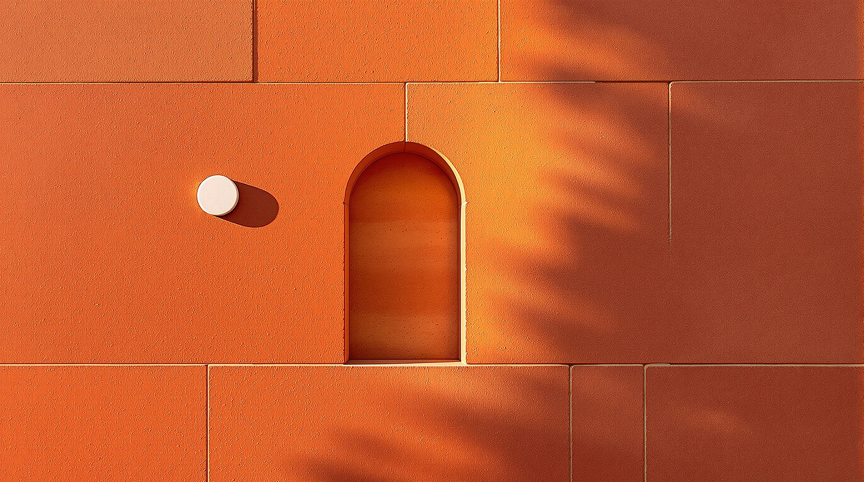 A section of the red sandstone outer wall of Jawahar Kala Kendra seen in raking afternoon light, the surface inlaid with a white marble planetary symbol, a small arched opening casting deep shadow, the stone glowing warm ochre-red