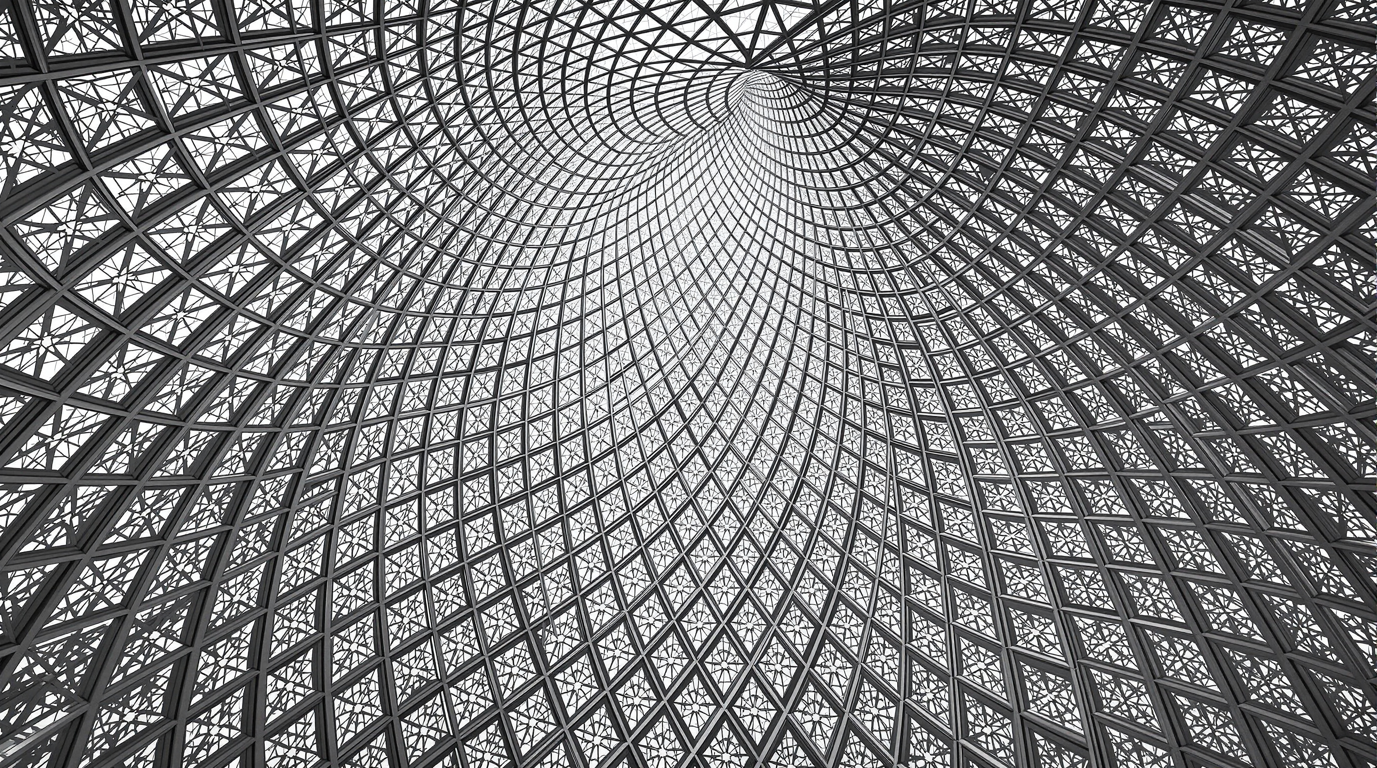 Looking straight up at the underside of the Louvre Abu Dhabi dome, the intricate silver star-and-cross lattice receding in eight overlapping layers, pierced by thousands of pinpricks of daylight against the shadowed steel