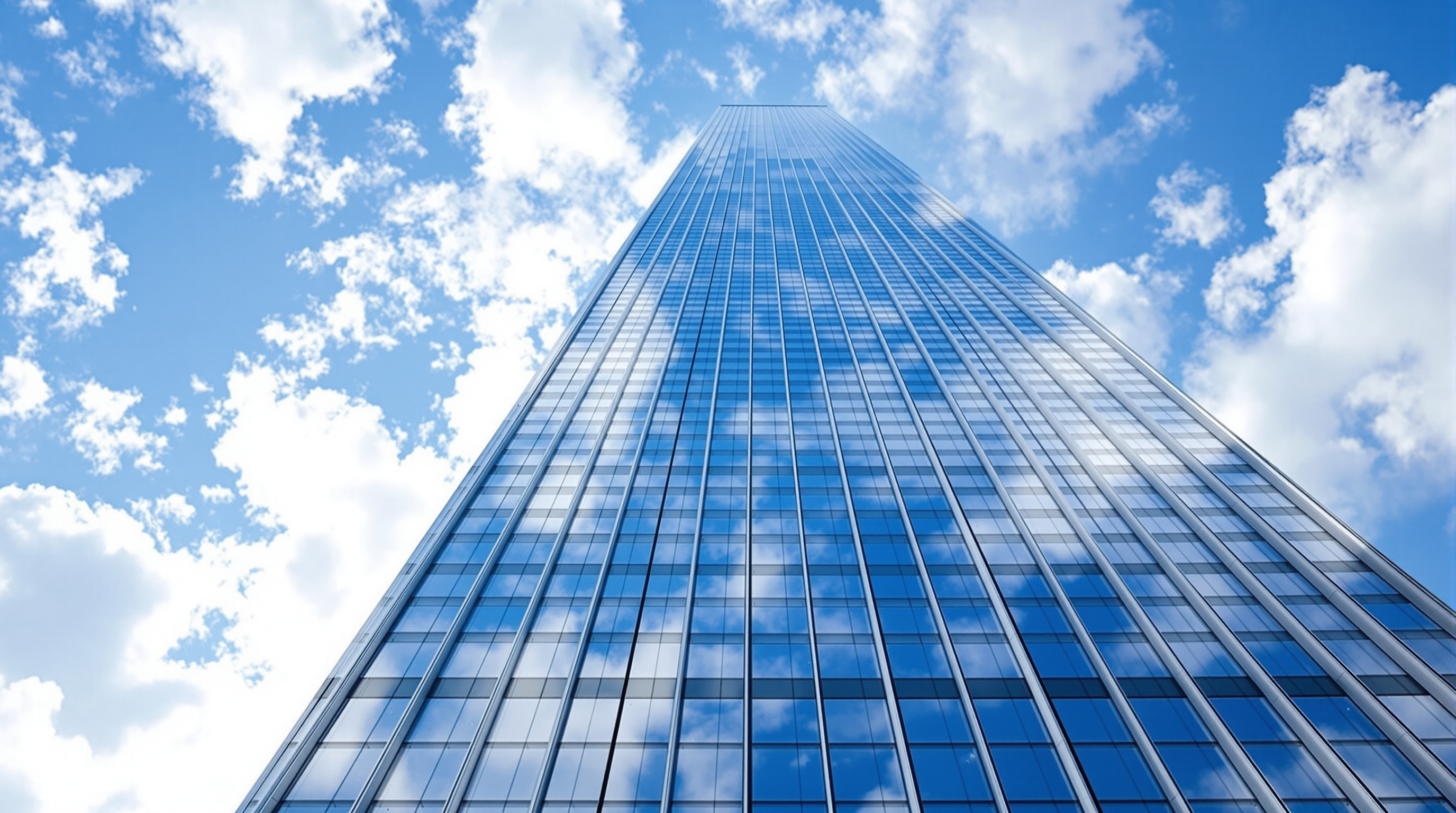 Looking straight up the sheer glass flank of One World Trade Center, the vertical mullions converging toward the sky, the surface alternating bands of blue-grey reflective glass that mirror passing clouds