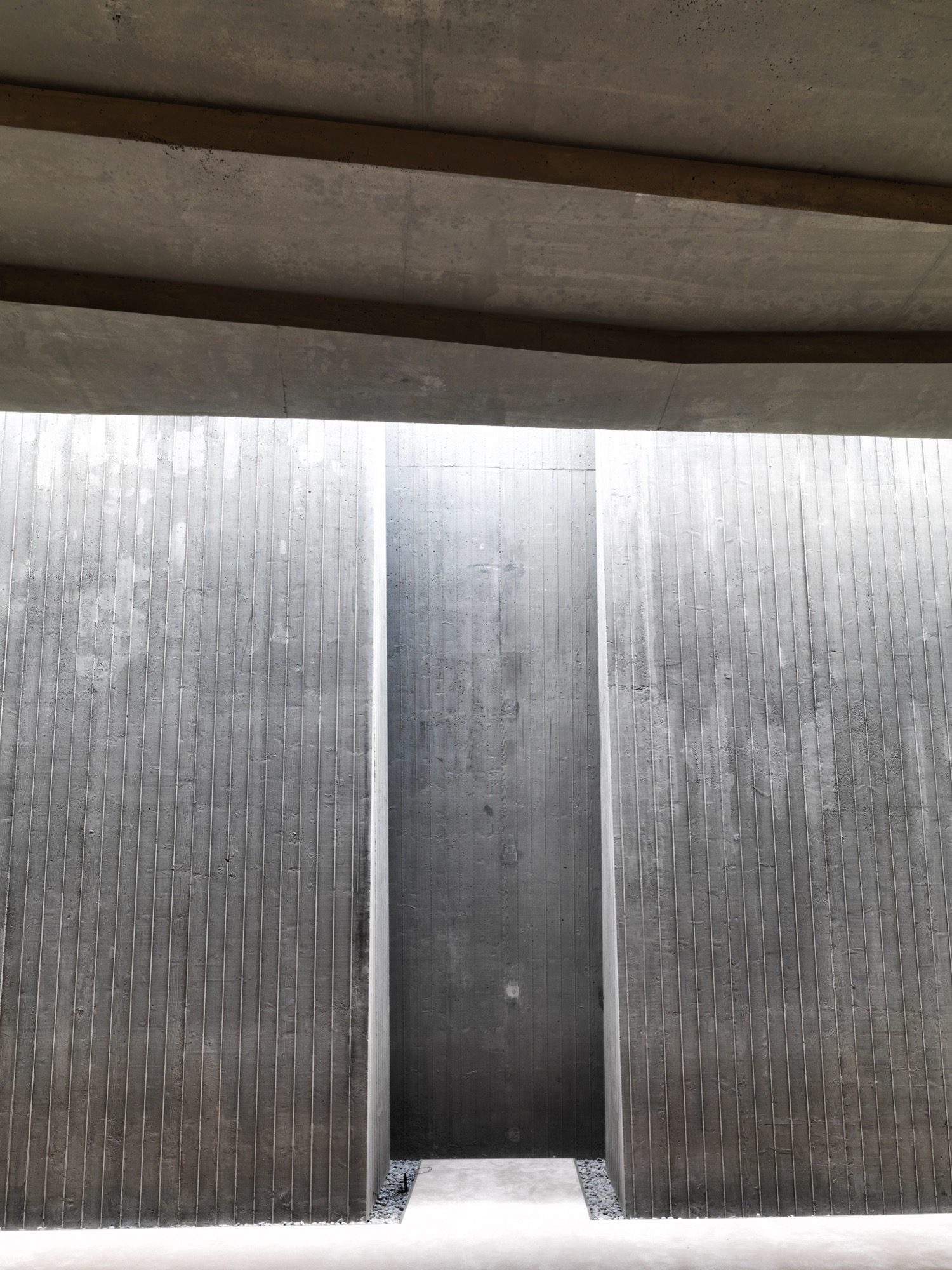 Detail of the board-marked concrete: a deep vertical fissure between two cast planes admits a blade of daylight into the dim hall — raw texture and light standing in for the ornament the mosque refuses