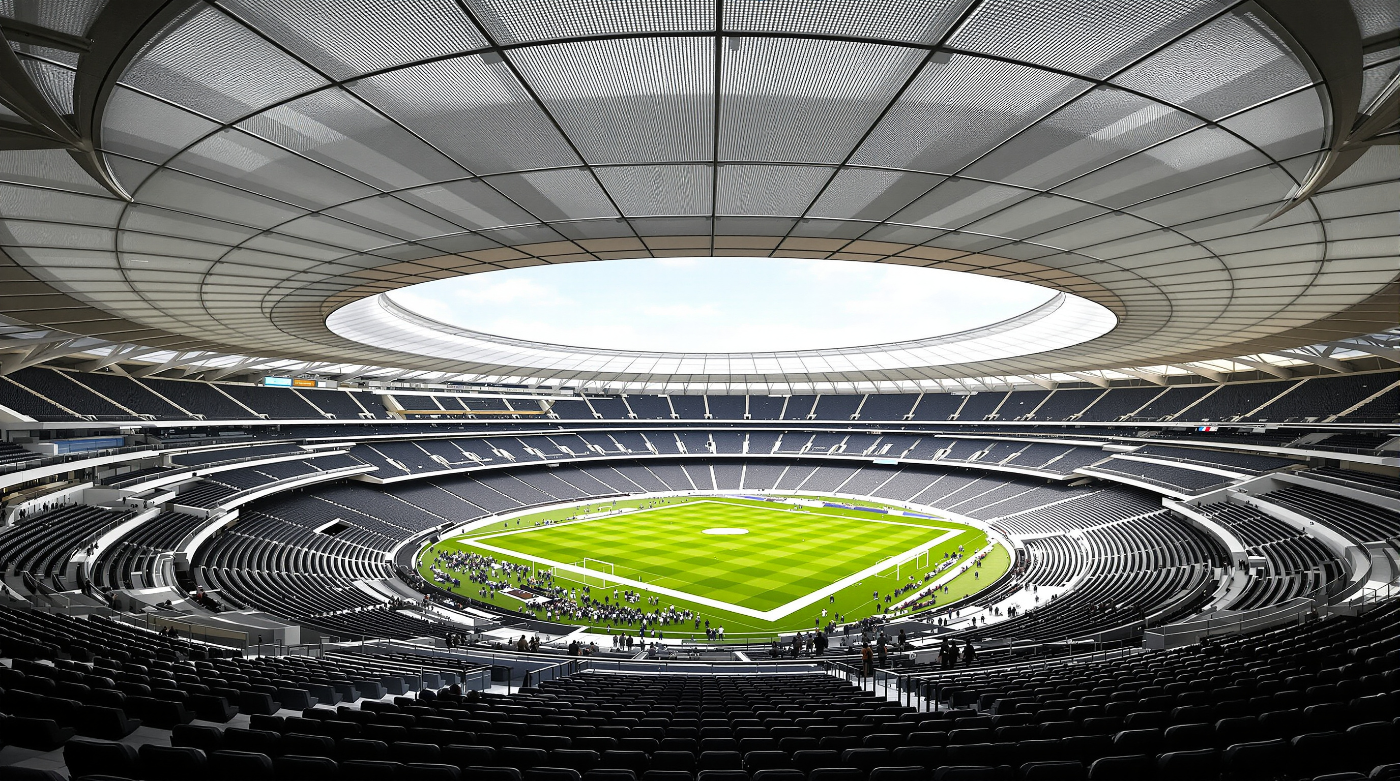 The interior bowl of SoFi Stadium seen from an upper terrace, tiers of seats descending steeply into the earth toward a green field, the translucent ETFE canopy glowing overhead and an open band of daylight visible at the roof's perimeter edge