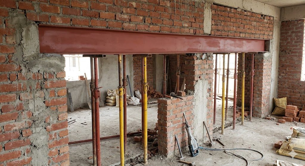 A real load-bearing wall opening on an Indian site: a steel I-beam lintel set into the masonry with full end bearing, adjustable steel props holding the slab from the floor below, and the new doorway being cut beneath the beam