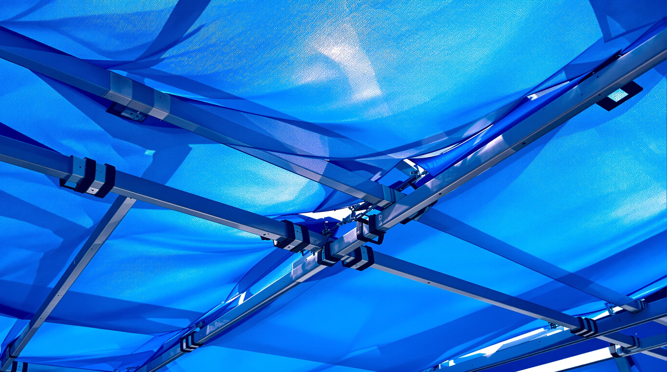 Detail of Wendy's tensioned blue nylon skin coated in titanium dioxide, the taut fabric catching sunlight where it stretches between scaffolding nodes, its matte photocatalytic surface reading as vivid electric blue against a summer sky