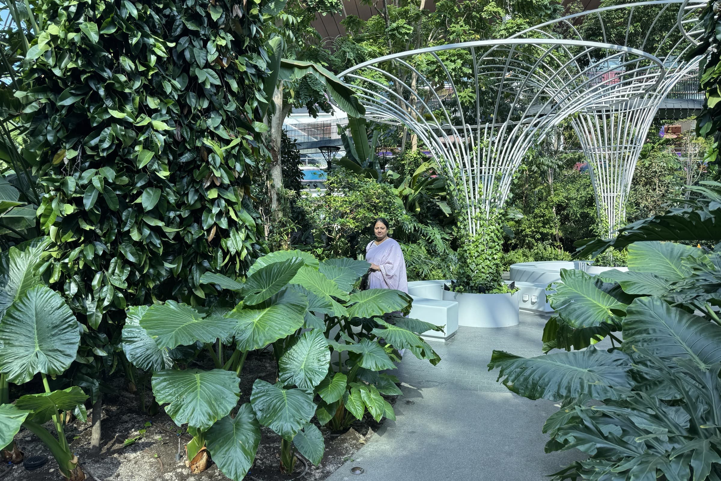 A visitor among the sculptural white tree-like canopy structures and tropical foliage of The Orchard at Doha airport