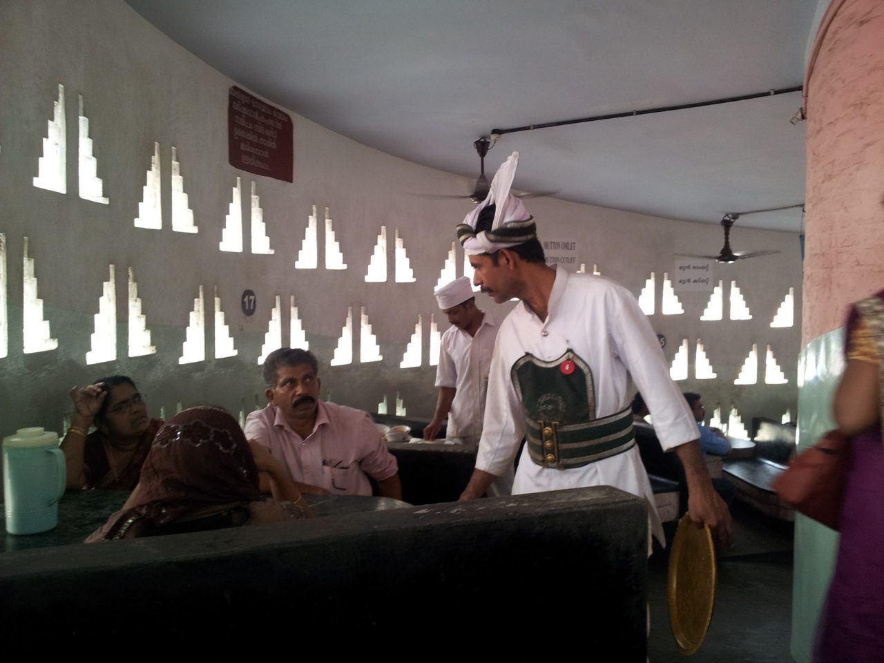 Inside the Indian Coffee House — a perforated brick jali screen filtering daylight over the counter and staff