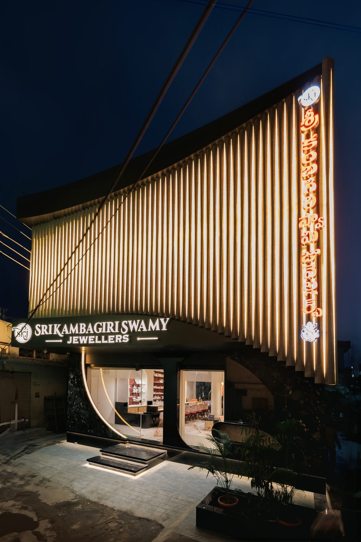 The lit facade of Sri Kambagiri Swamy Jewellers at night, its vertical fins glowing