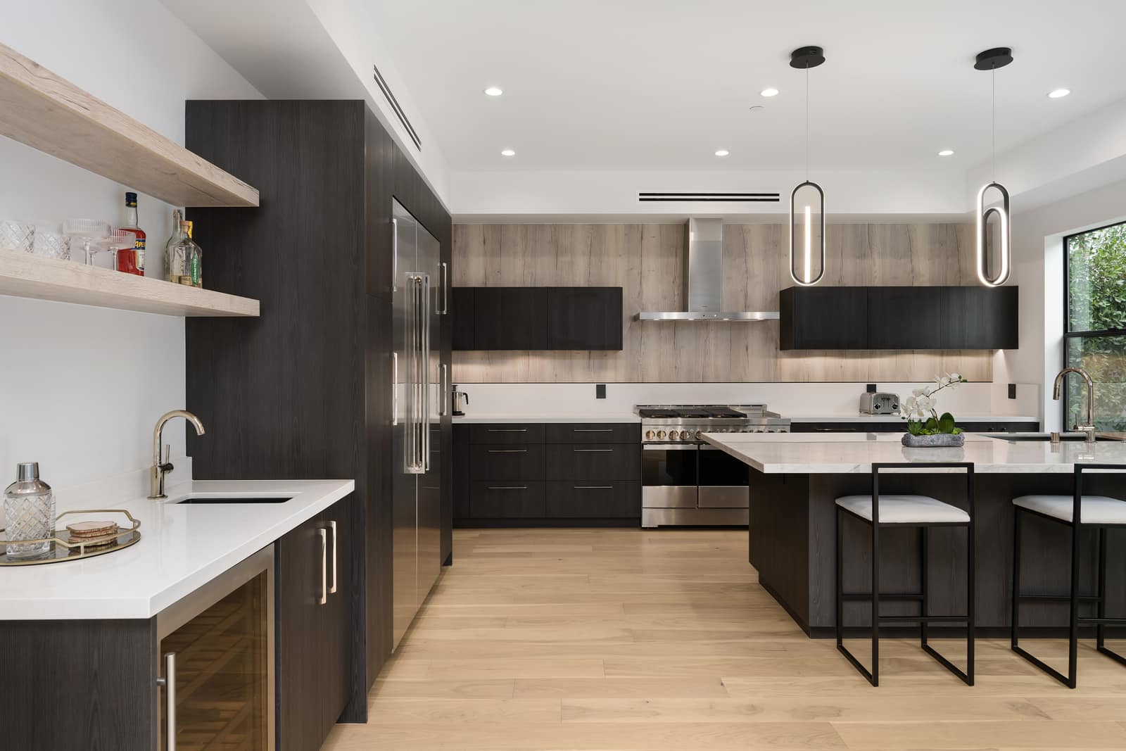 A finished, well-lit modern kitchen with an island and bar stools, dark and pale wood cabinetry and a stone countertop, photographed at the end of its build