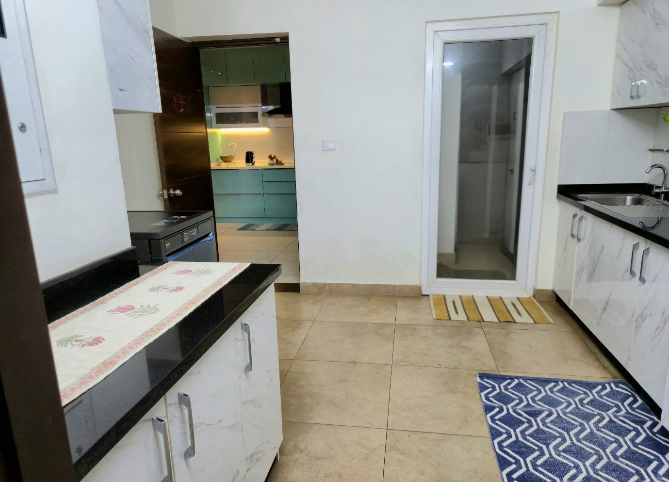 The doorway between the two kitchens — glossy blue cabinetry on one side, marble-patterned white and a black counter on the other