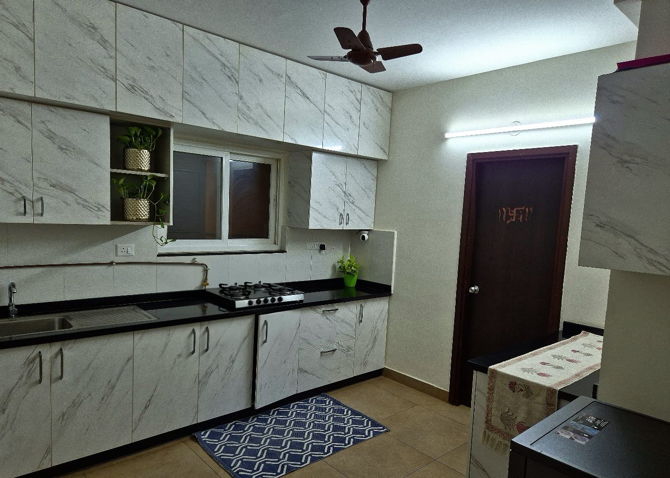 The second kitchen — marble-patterned white shutters, a black countertop and a compact working wall around the sink, window and cooktop