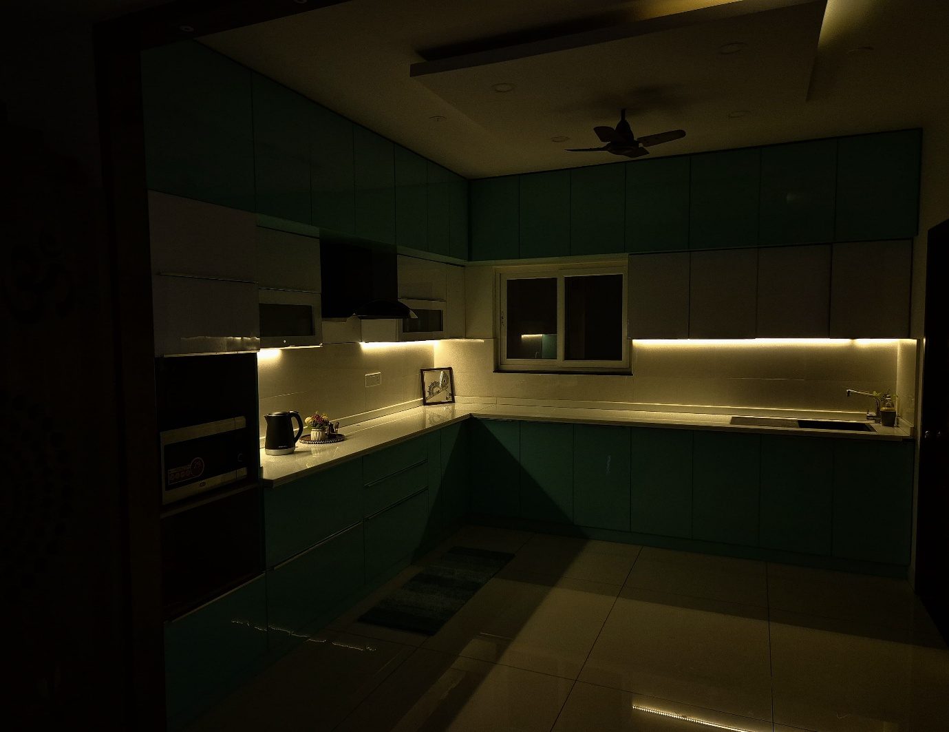 The blue kitchen in lower light, the warm under-cabinet strip drawing a horizontal line above the countertop