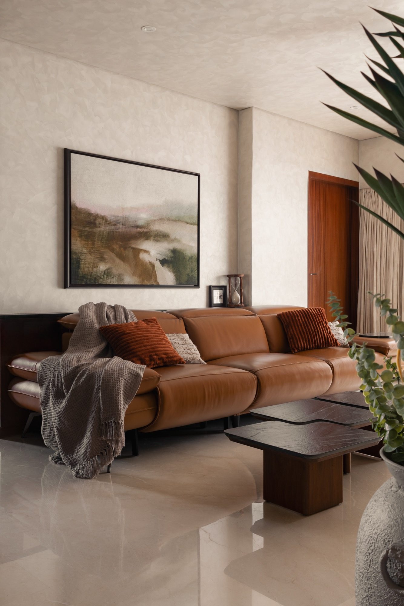 Cognac leather recliner against textured plaster, a landscape artwork above and a dark timber bar unit alongside