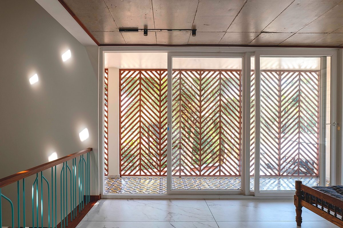 An upper room looking through a wide glazed opening to the balcony and its diagonal timber screen, with wall lights and a turquoise balustrade