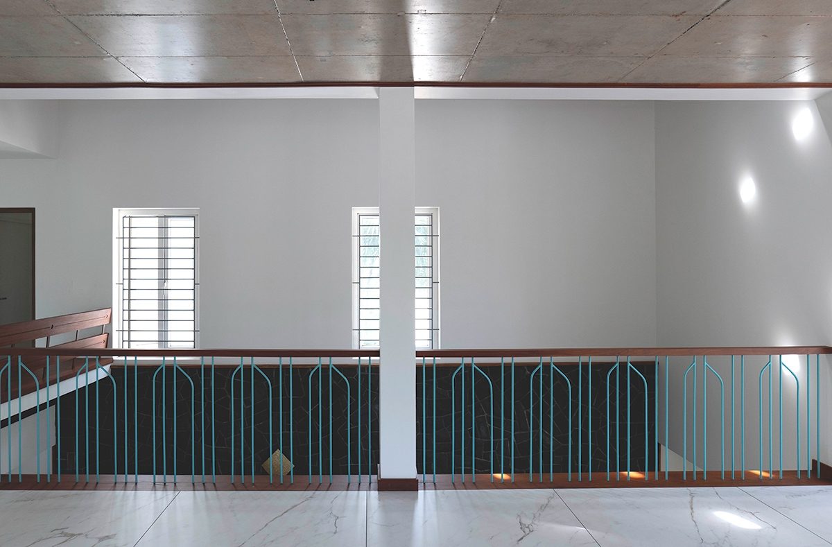 Across the upper passage — a pale wall with patches of light and two tall windows, a turquoise balustrade, a veined floor and a timber ceiling