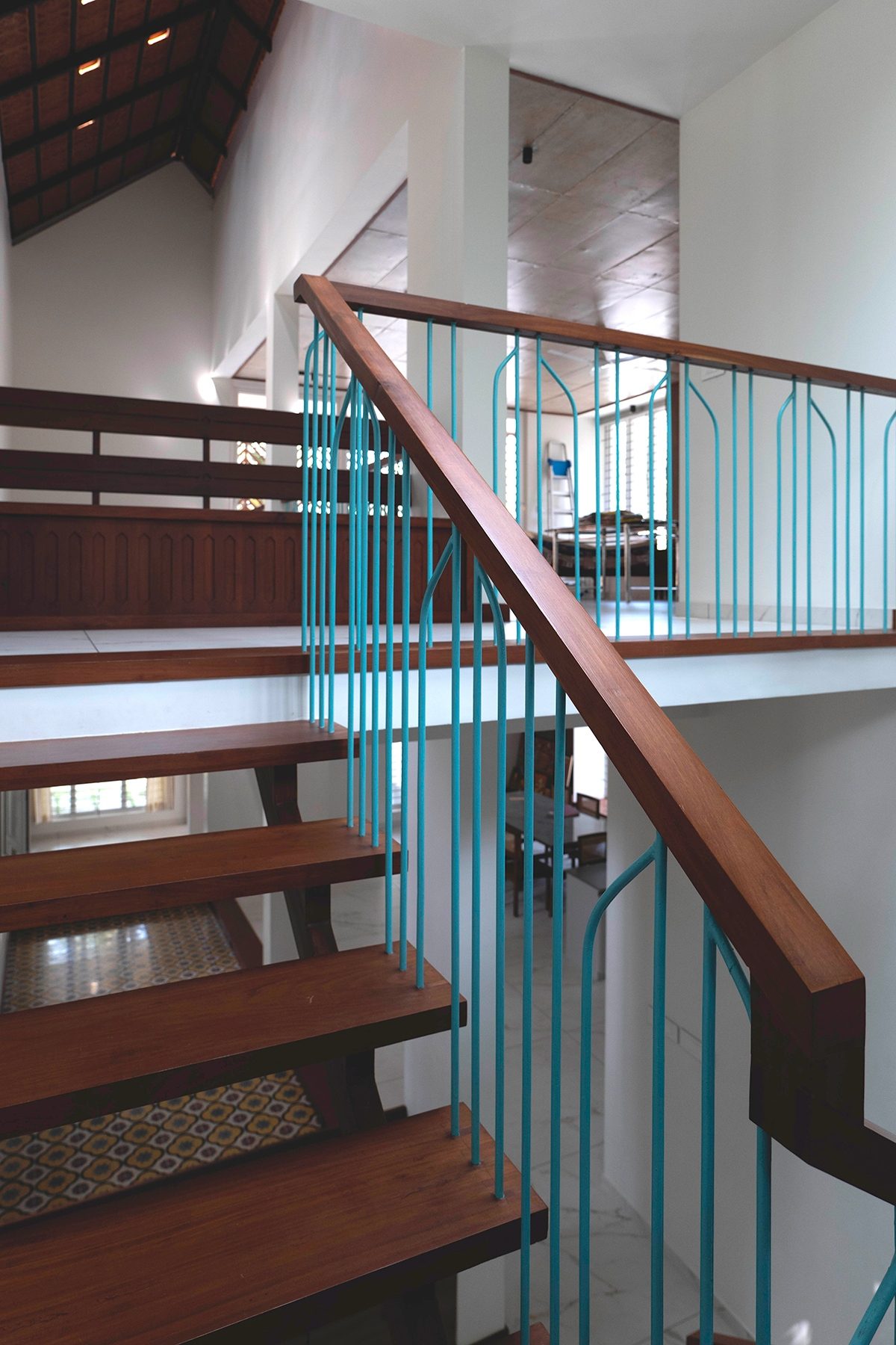 The open-tread timber stair with its turquoise-and-timber handrail rising to the upper passage
