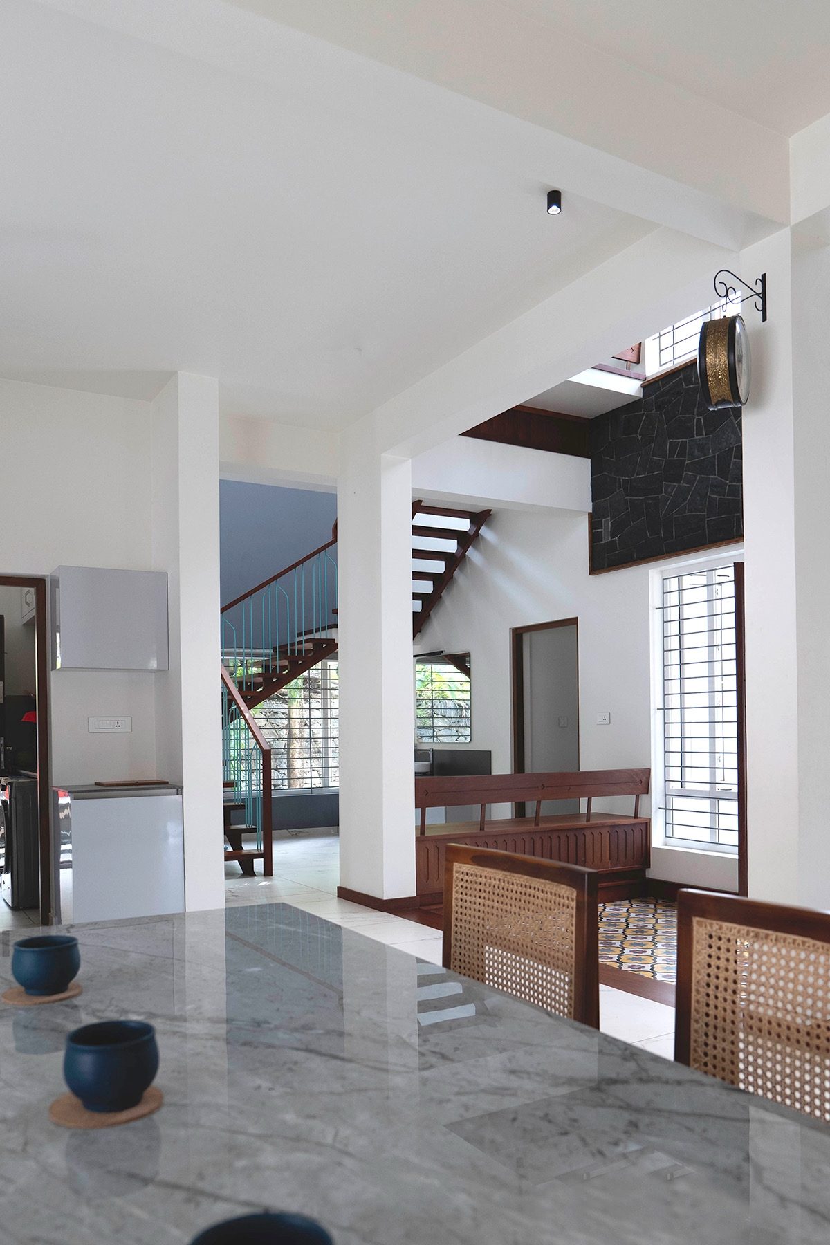 From the dining area toward the central court — the stone-topped dining table, cane-backed chairs, an illuminated ceiling fitting and the stair beyond
