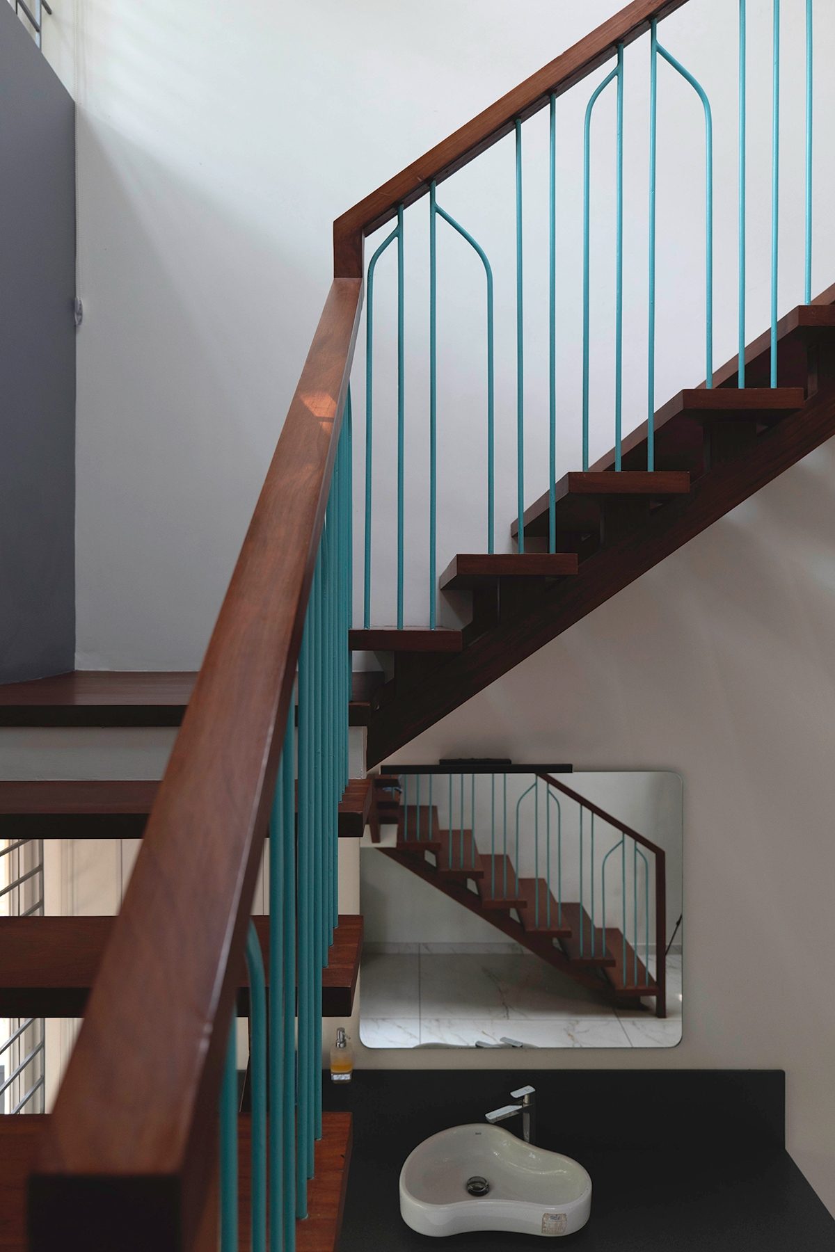 A close view of the stair — timber treads and a turquoise-and-timber handrail, with a mirror and wash basin beneath reflecting the flight