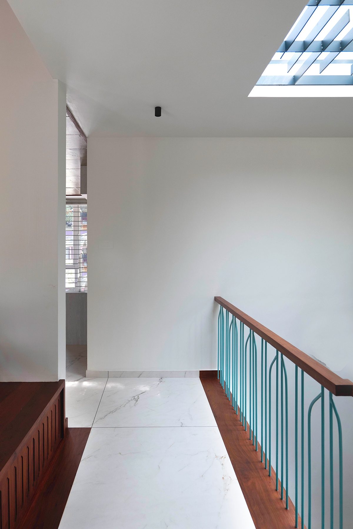 The upper landing beside a turquoise balustrade, with a rectangular opening overhead and a pale wall