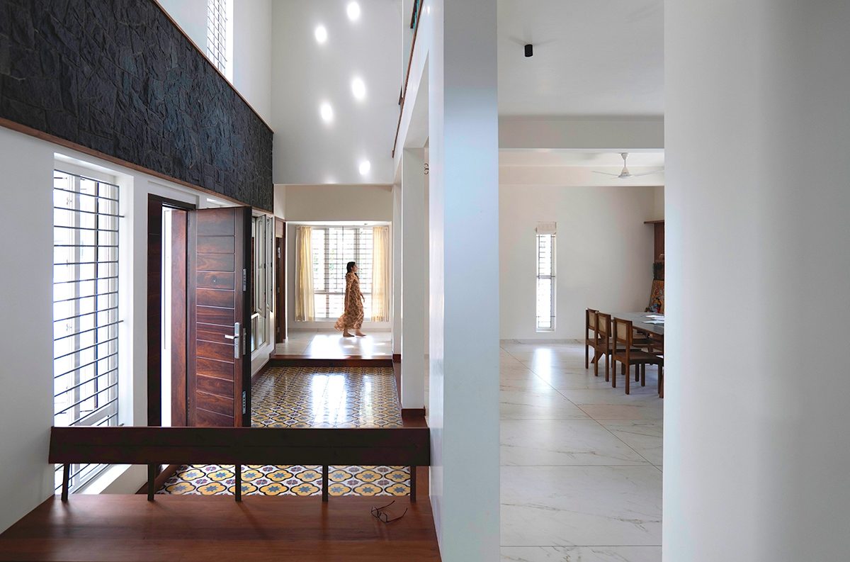 Seating beside the patterned-tile floor of the central court, a tall pale wall with patches of light, a black stone wall above, and the dining area beyond