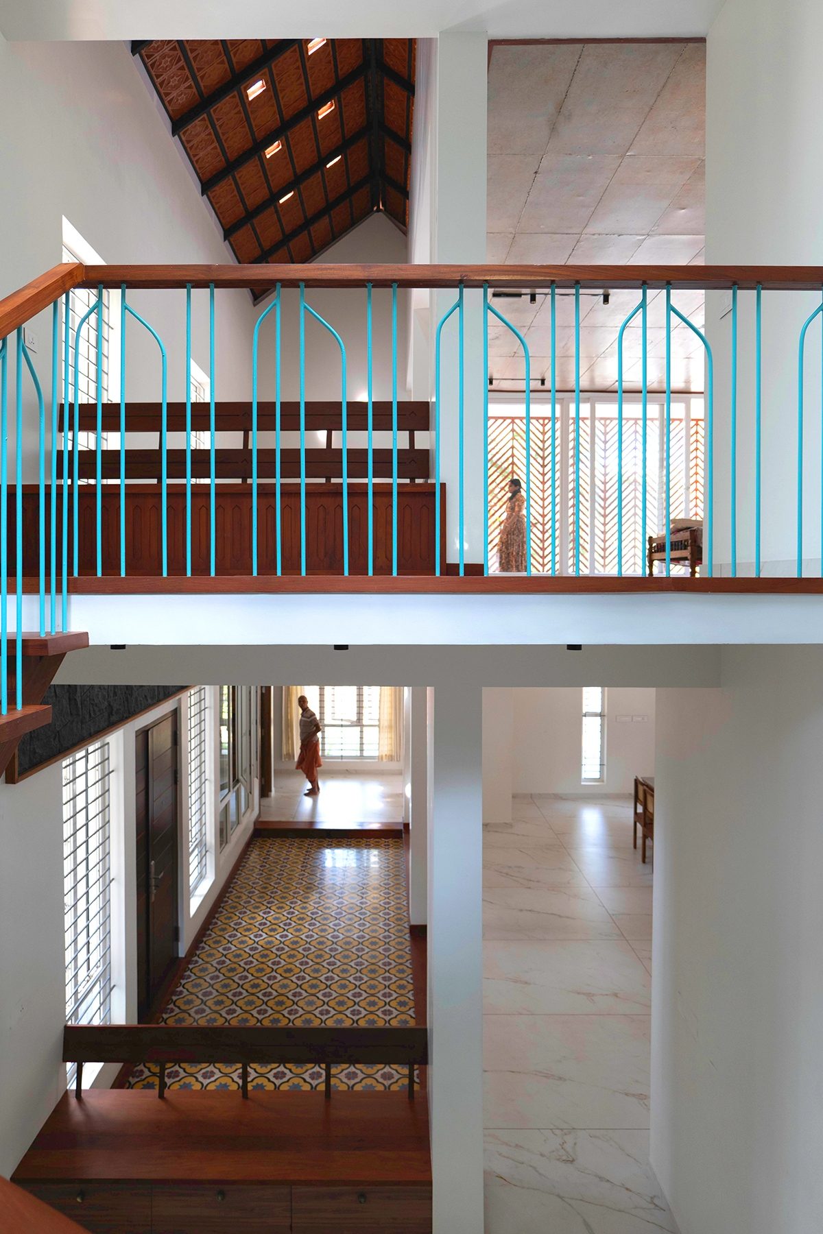 Looking across the central volume — turquoise balustrade and upper passage above, roof openings in the timber roof, and the patterned floor below