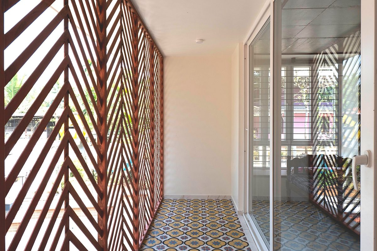 The upper balcony behind a timber screen of repeated diagonal members, with a patterned-tile floor and glazed sliding doors