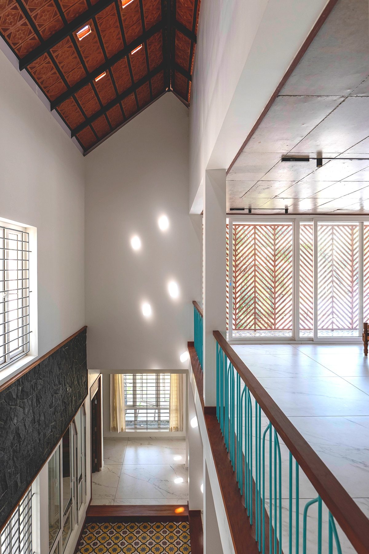 View down from the upper passage — bright patches of sunlight on the tall wall beside the central court, the timber roof above and the floor below