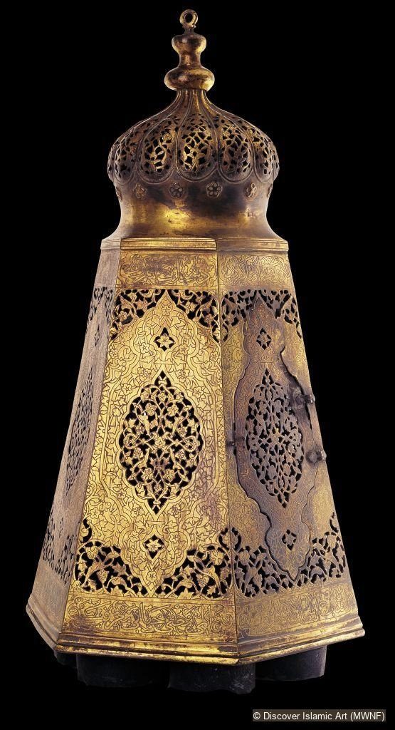 A tall hexagonal pierced and chased brass lamp with a domed, perforated top, photographed against a black background