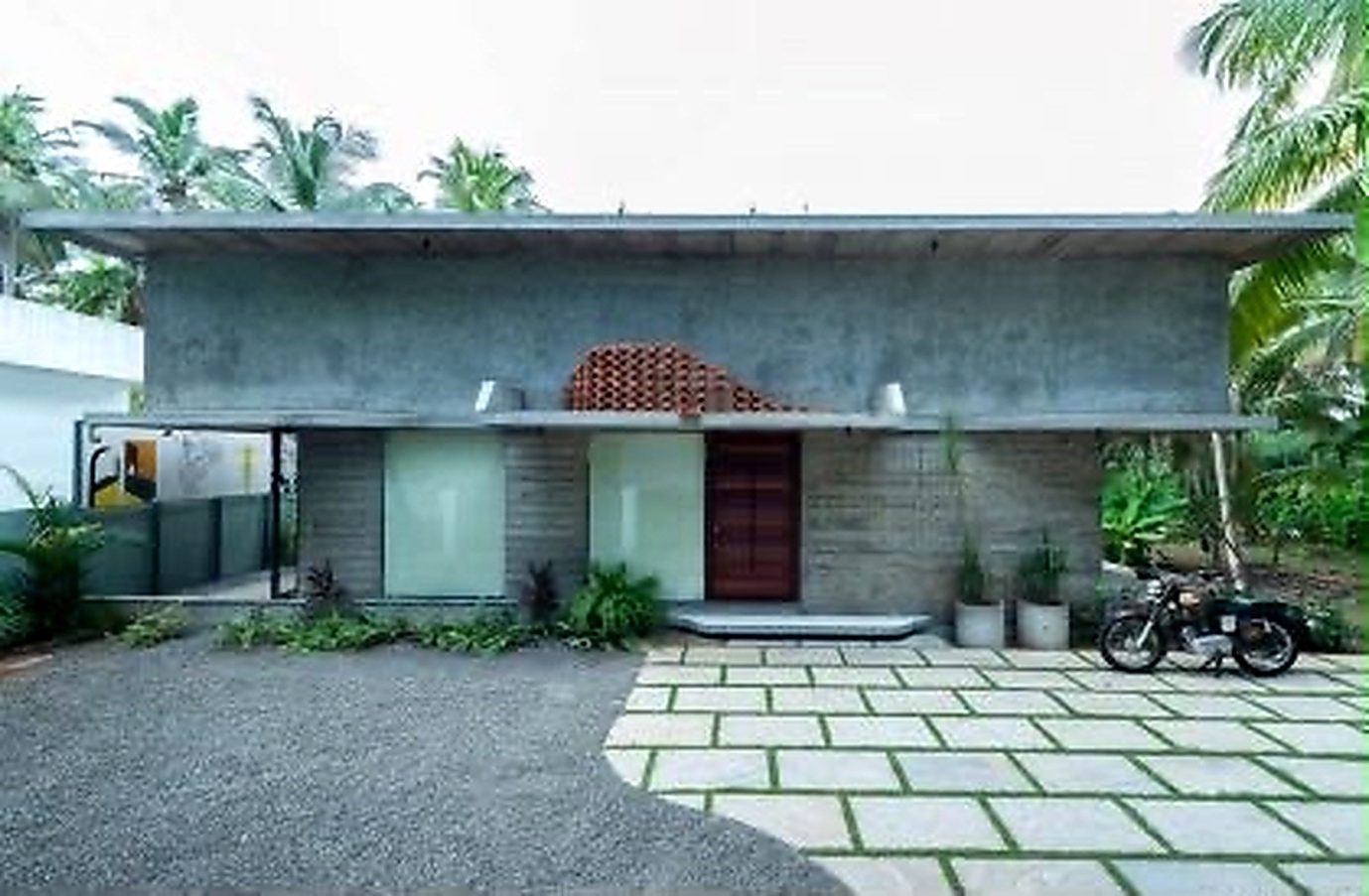 The Violet Office exterior — a broad concrete roof plane over glazing, a timber entrance door and a paved forecourt among coconut palms