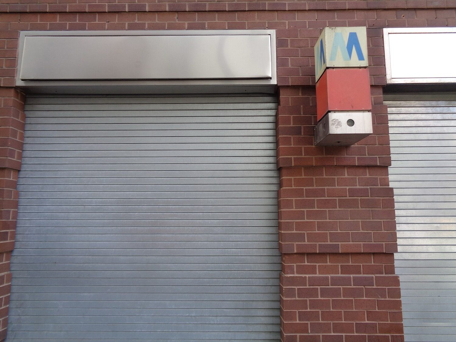 A steel rolling shutter at a shopfront — interlocking laths rolling onto a drum.